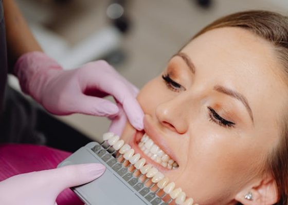 A woman sits in a dental chair while a dentist cleans her teeth with dental tools.