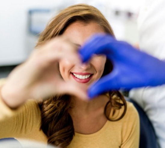 A person with wavy brown hair wearing a yellow sweater is receiving care from a person in a medical setting, wearing blue gloves.